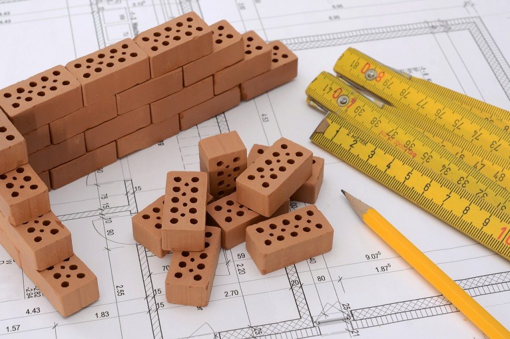 briques miniatures, mètres et crayon à papier posés sur un plan de construction